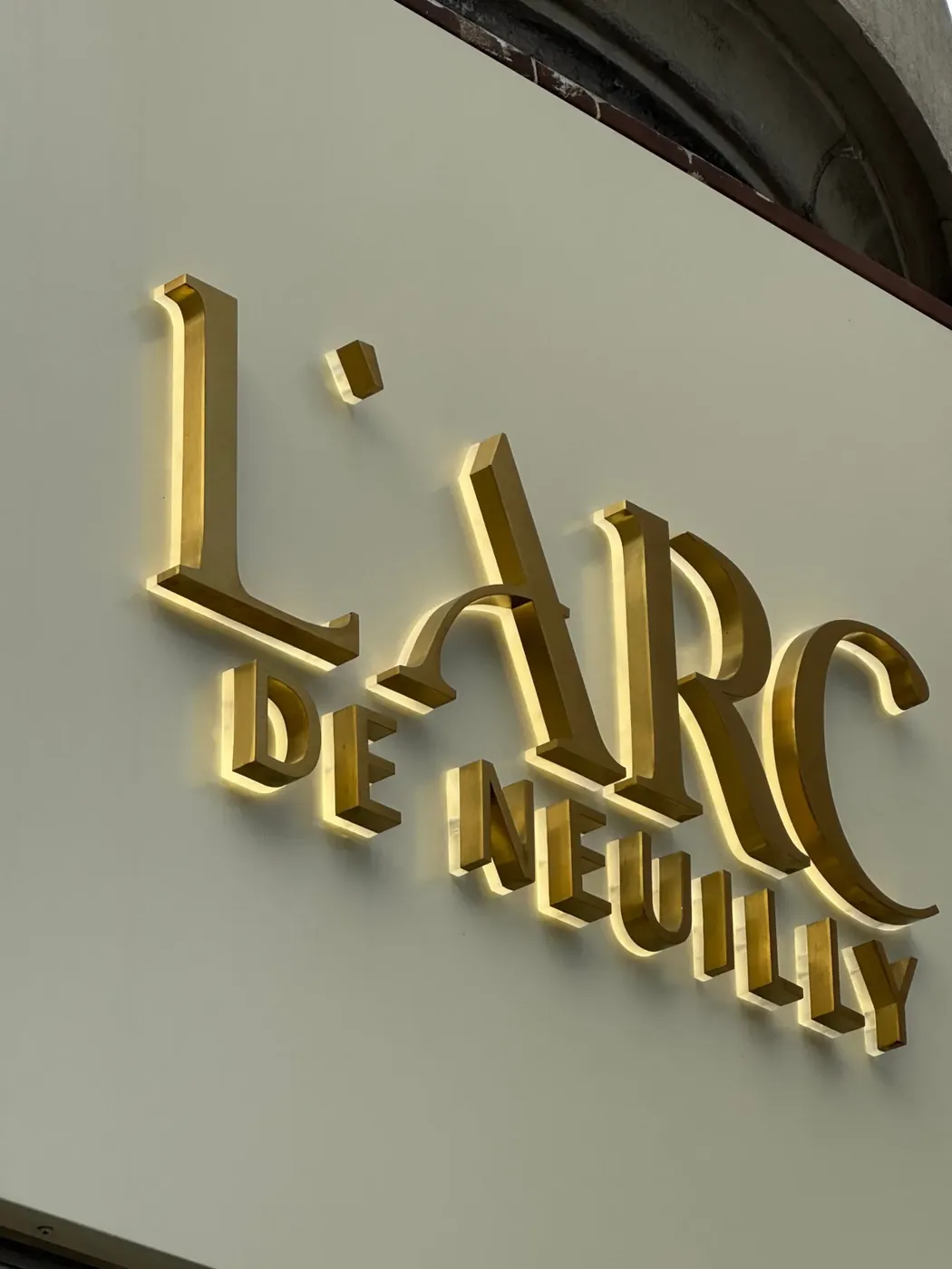 Enseigne L’Arc de Neuilly, lettres lumineuses en laiton brossé rétroéclairées, par LADONNA