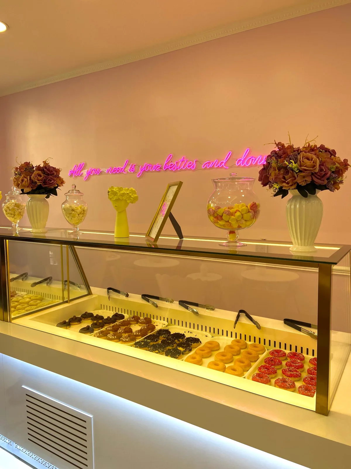 Phrase en néon rose All you need is your besties and donuts au-dessus d’une vitrine de donuts chez Besties Bakery, Paris 9e, par LADONNA