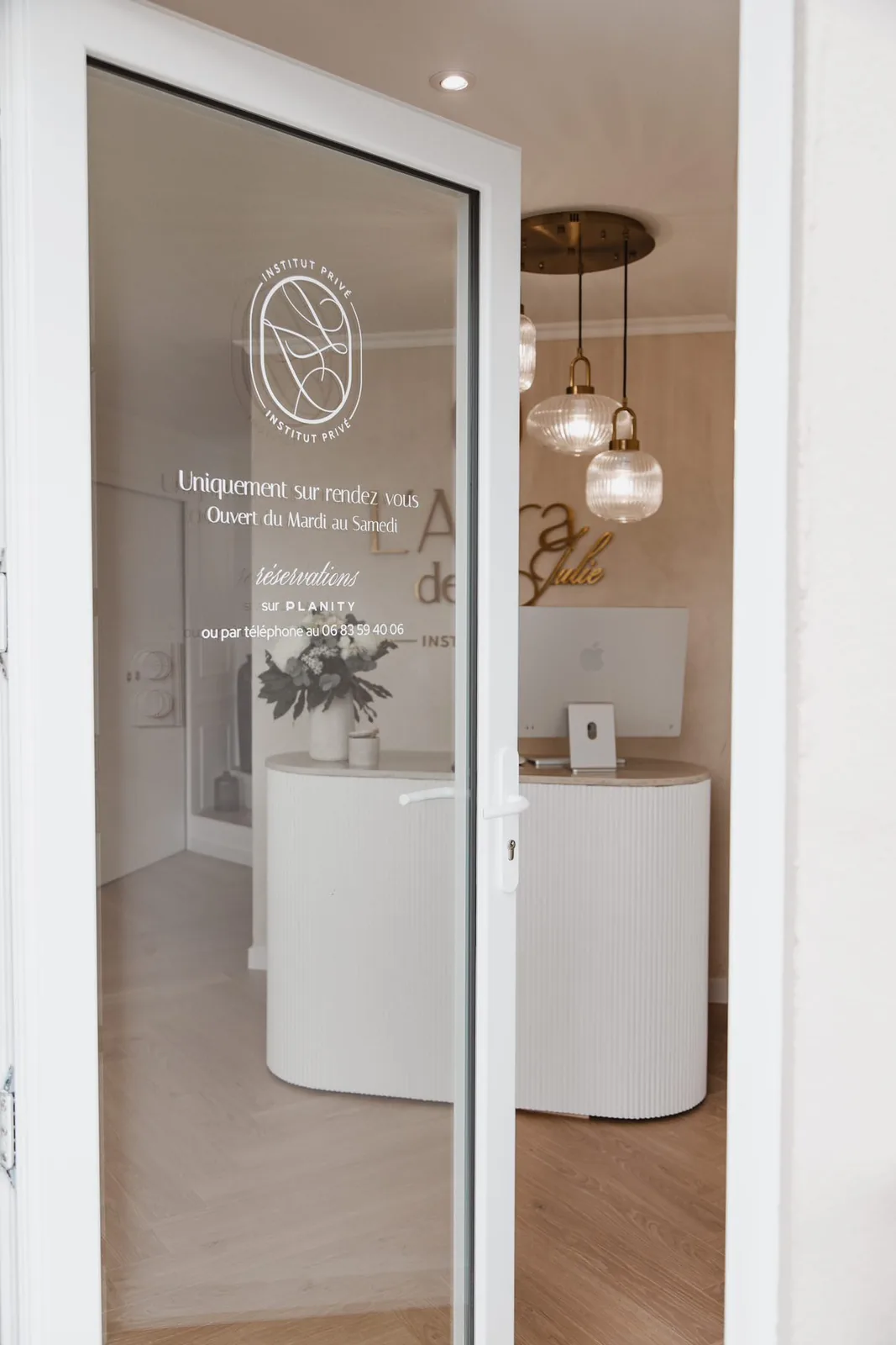 Porte vitrée de L’Aura de Julie à Cusset avec logo, horaires et réservations en lettrage blanc, par LADONNA